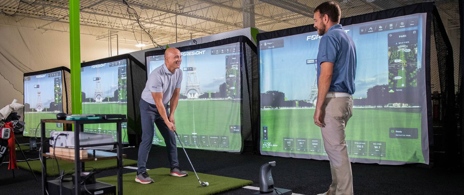 Two golfers in the RYP Academy simulator bay, Foresight screens showing live ball data