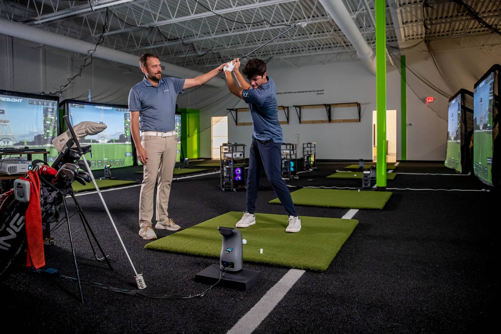 A coach and a junior golfer working through a swing in the wide training bay