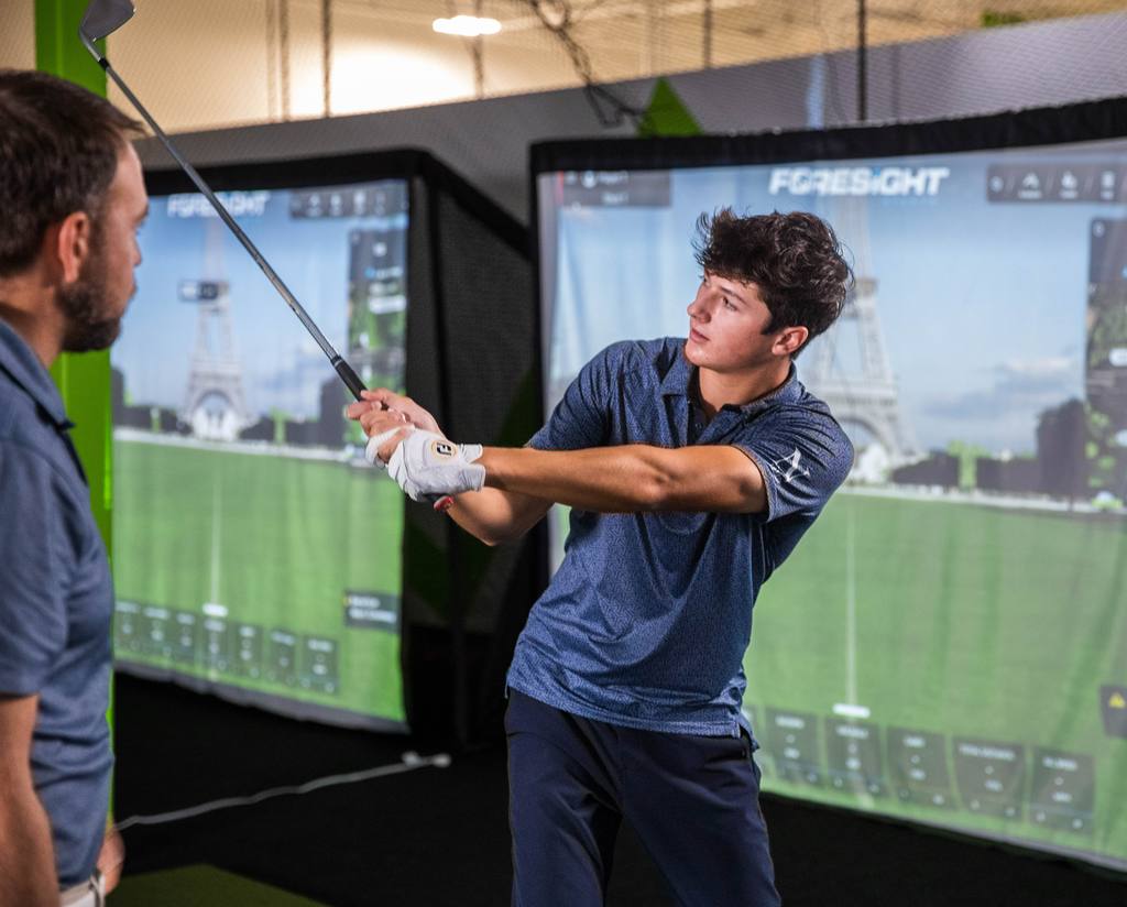 A junior golfer through impact, with the Parallax analysis overlay tracing swing plane, spine angle and shoulder line