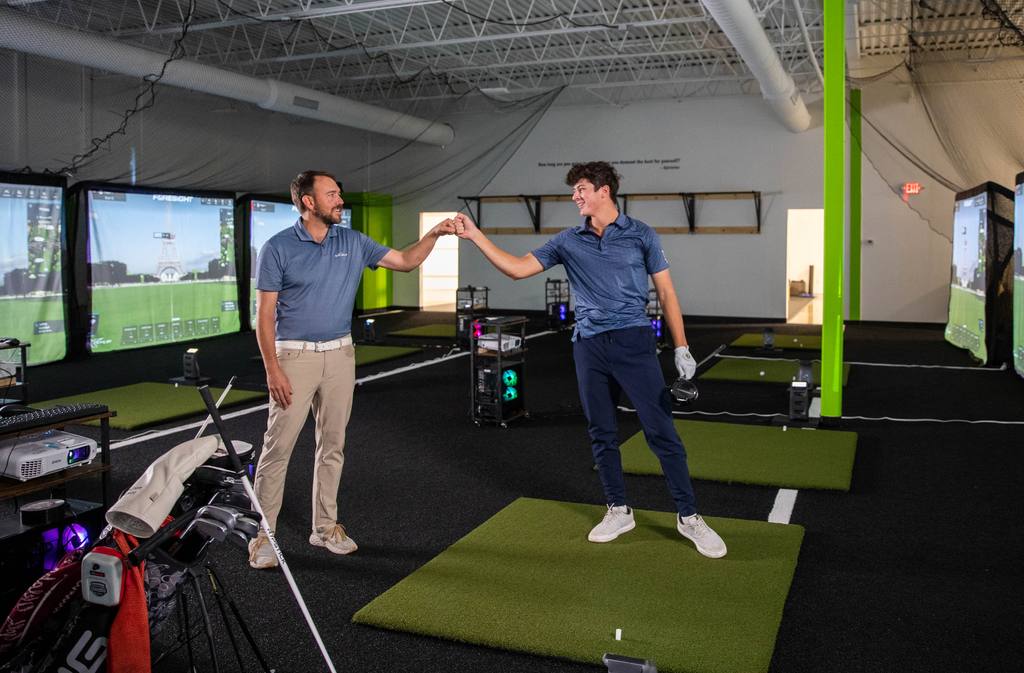 A RYP Academy coach and a junior golfer bumping fists after a rep in the training bay